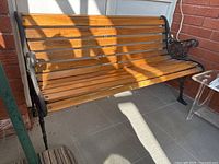 Full view of the garden bench showing solid wooden slats and cast iron side panels with decorative floral design and curved armrests.