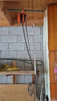 Tiger 1 Ton orange chain hoist mounted on ceiling beam with metal chains and hook hanging down, setting in workshop or garage area