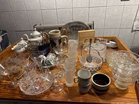 Wide view showing the grouping of vintage glassware and ceramics on wooden surface against tiled wall, including cups, bowls, plates, and serving pieces.