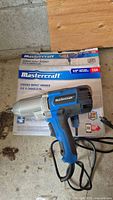 Mastercraft corded impact wrench with power cord next to original boxed packaging on wood surface.