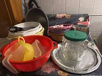 Full view of assortment showing colander, measuring cups, glass jar, trays, baskets, mixing bowls, and skillet arranged on tiled countertop.