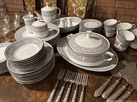 Full lot overview showing plates, bowls, cups, teapot, sugar bowl, creamer and flatware on table.