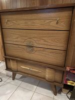 Front view of vintage 4 drawer dresser showing design details and wood grain finish.