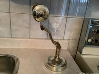 Front side view of the metal bankers lamp showing the base, adjustable arm, and round back reflector of the shade.