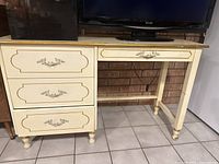 Full view of vintage cream-colored solid wood desk with three drawers and gold detailing, along with matching chair.