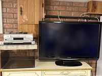 Sharp television and stack of Sylvania VCR and GoldStar DVD player on cabinet, showing overall lot contents