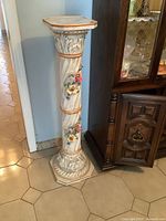 Full view of tall ceramic pedestal with octagonal top and base placed on tiled floor beside wooden cabinet.