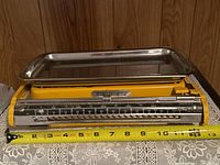 Front view of vintage yellow weigh scale with metal tray and tape measure showing length of about 12 inches.
