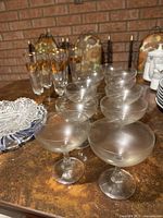 Wide shot showing frosted coupe glasses in front, cut glass dish to left, and gold-trimmed tall glasses behind.