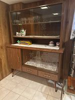 Full view of vintage mid-century china cabinet showing wood finish, glass doors with glass shelving inside upper compartment, lace liners, lower section with display glass door, cupboard door and two drawers.