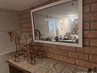 Photo showing the rectangular mirror mounted on a brick wall above a counter with the rattan horse-shaped vase stand next to it.