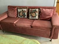Front view of vintage pink velvet 3-seater sofa bed with two floral needlepoint cushions on seat cushions.