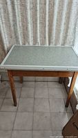 Front view of the vintage table showing the laminated top and wooden legs on tiled floor with curtain background.