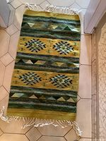 Full view of the rectangular Kilim rug with visible fringe on both ends, displaying the geometric pattern in green, yellow, and contrasting colors.