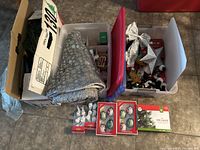 Photo showing assorted Christmas ornaments including owl and bird designs, a tree skirt with snowflake pattern, and small figurines in clear plastic bins and boxes.