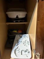 View of stacked metal baking pans with white silicone molds on top inside a wooden cabinet.