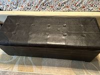 Top view of the black leather-look tufted storage ottoman showing the textured surface and button tufting.