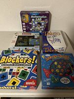 Front view of the 5 game boxes: Mathematics LAB, Taboo, Bloxels, Blockers, Let's Go Fishin'. Boxes are colorful and labeled.
