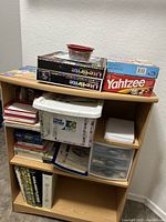 Shelf containing multiple board games such as Yahtzee and Lite-Brite, plastic drawers, binders, and a container