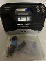 Front view of BONAIRE digital inflator with visible handle, digital display panel, and included inflation nozzles in a plastic bag.