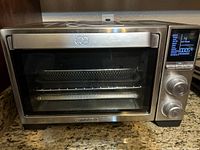 Front view of the Calphalon stainless steel air fryer oven showing mesh basket inside and digital display with control knobs on right.