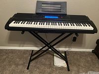 Full view of Casio electronic keyboard on X-frame stand showing 76 keys and sheet music stand.