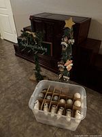 Photo of decorated wooden stocking holder with greenery and chalkboard sign, plastic storage container with various white and silver ball and animal figure ornaments organized in compartments