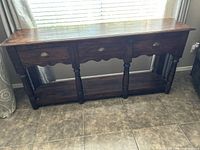 Full front view of the dark brown wooden console table with three closed drawers and turned legs.