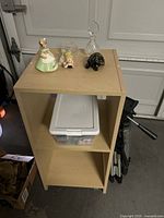 Full lot showing top of cabinet with figurines and glass decanter, plastic bin in shelf below, tripod stand to side