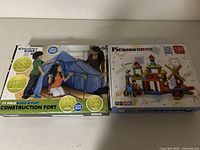 The boxed Discovery Kids Construction Fort 77-piece set and Picasso Tiles 120-piece set boxes side by side, showing packaging artwork and set counts.