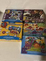 Five boxed educational games and puzzles arranged on floor including Mathematics Lab, Counting Treasures, Exploring Space, Dinosaur Book & Puzzle, and Wiggle Eyes Puzzle
