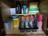 Photo of shelf with assorted Tupperware containers, metal water bottle, plastic pitchers, and stacked red disposable cups.
