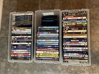 Three clear plastic storage bins filled with assorted DVDs in standard cases with visible titles like Jackass The Movie, The Patriot, and 8 Mile.