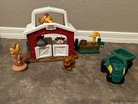 Full view of Fisher-Price Little People farm playset items including barn, animal figures, tractor attachment, water trough and cornstalk accessory on floor.