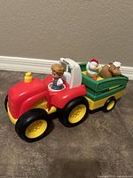 Photo showing red and yellow Fisher-Price Little People toy tractor with farmer figure seated and attached green and yellow trailer.