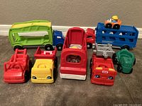 Overview of multiple Fisher-Price colorful plastic toy vehicles including car carrier, dump trucks, bus, fire truck, and cement mixer.