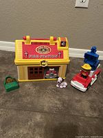 Full view of Fisher-Price Fire Station building, fire truck with fireman figure, dog figure, and accessories on floor.