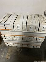 Stack of 10 white cardboard boxes containing Florida Tile ceramic wall tiles, stacked 2 rows high on a concrete floor. Box shows part of the tile surface with subtle beige/tan design.