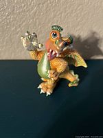 Front view of green and orange dragon figurine holding a large clear crystal orb.