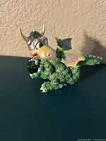 Front side view of the green dragon figurine holding a large green Swarovski crystal with detailed eyes and purple wings.