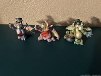 Front view of three Franklin Mint Mood Dragons porcelain figurines, detailed colorful dragons with props, hats, and Swarovski crystal decorations.