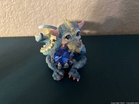 Front view of the blue dragon figurine holding a large blue crystal, showing its detailed face, claws, and scales