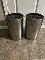 Two stainless steel cylindrical waste bins side by side showing perforated pattern and overall condition