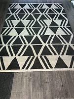 Full view of the rectangular geometric patterned rug on dark wood flooring, showing the repeating black and white triangular shapes with striped details.
