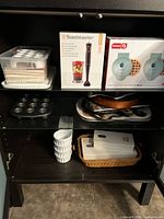 Photo of kitchen appliance and bakeware set stored on shelves, showing boxed hand blender, waffle makers, cake pop pans, ramekins, and some trays.