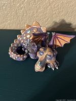Close-up photo of a purple and beige moss dragon porcelain figurine with Swarovski crystals visible on the body and the dragon curled with details on its face and wings.