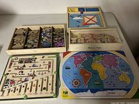 Photo showing five wooden puzzles including wooden storage boxes, boat and animal-shaped puzzles, mixed pieces in compartments, a colorful world map puzzle, and a wooden maze puzzle with balls.