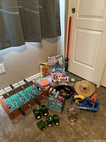 Overall view of the mixed toy collection on floor including foosball table, toy trucks, cowboy hat, lightsaber, and other toys