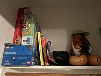 Shelf with LEGO DUPLO and City sets stacked on left, three children's books standing upright in middle, and Mr. Potato Head toy disassembled with parts on right.