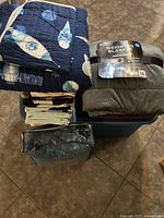 Photo of folded navy space-themed quilt on top of a stack of other quilts, weighted blanket folded with label visible, and storage tote below them.